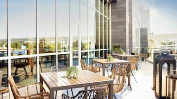 An outdoor patio area with tables and chairs, large windows, and a view of the cityscape.