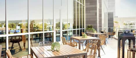 Un patio al aire libre con mesas y sillas, amplias ventanas y vistas a la ciudad.
