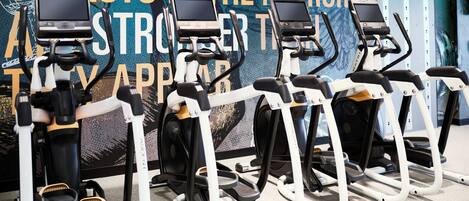 Varias bicicletas estáticas en un gimnasio, con un cartel grande al fondo.