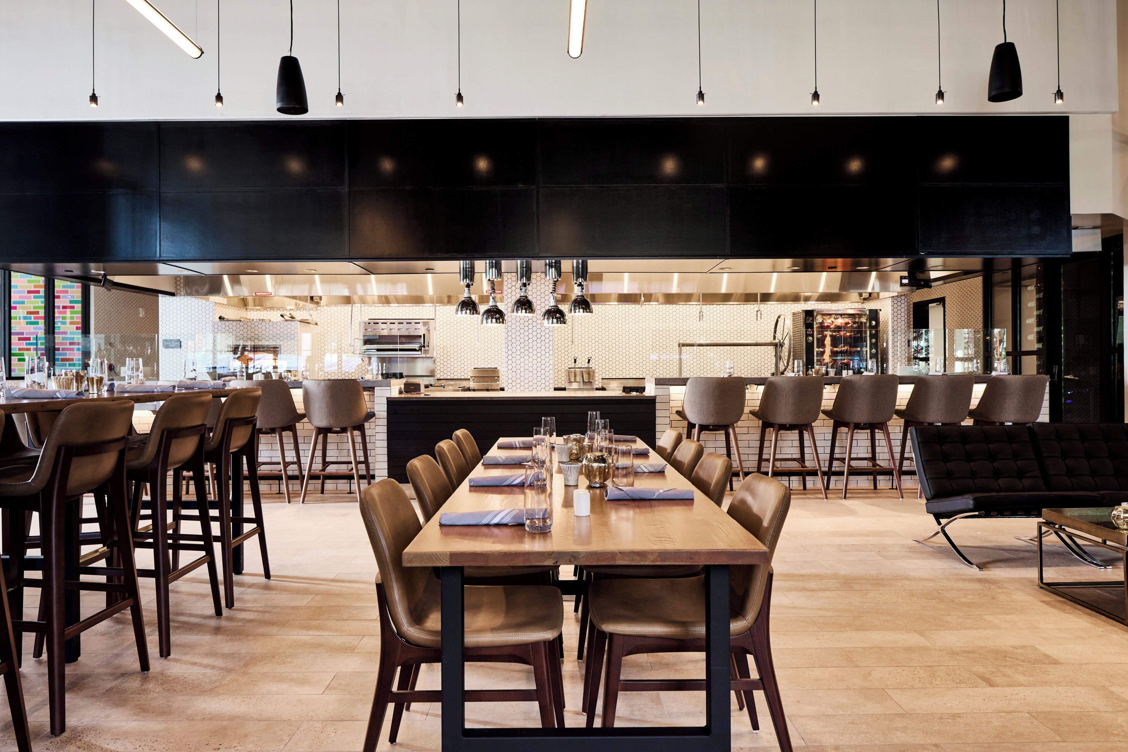A modern dining area with a long wooden table, multiple chairs, and pendant lighting.
