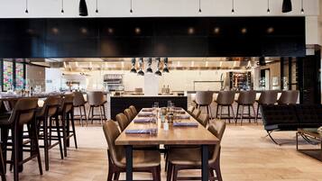 A modern dining area with a long wooden table, multiple chairs, and pendant lighting.