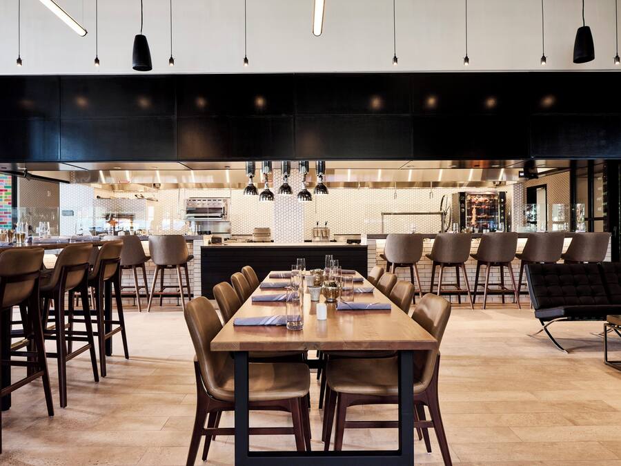 A modern dining area with a long wooden table, multiple chairs, and pendant lighting.