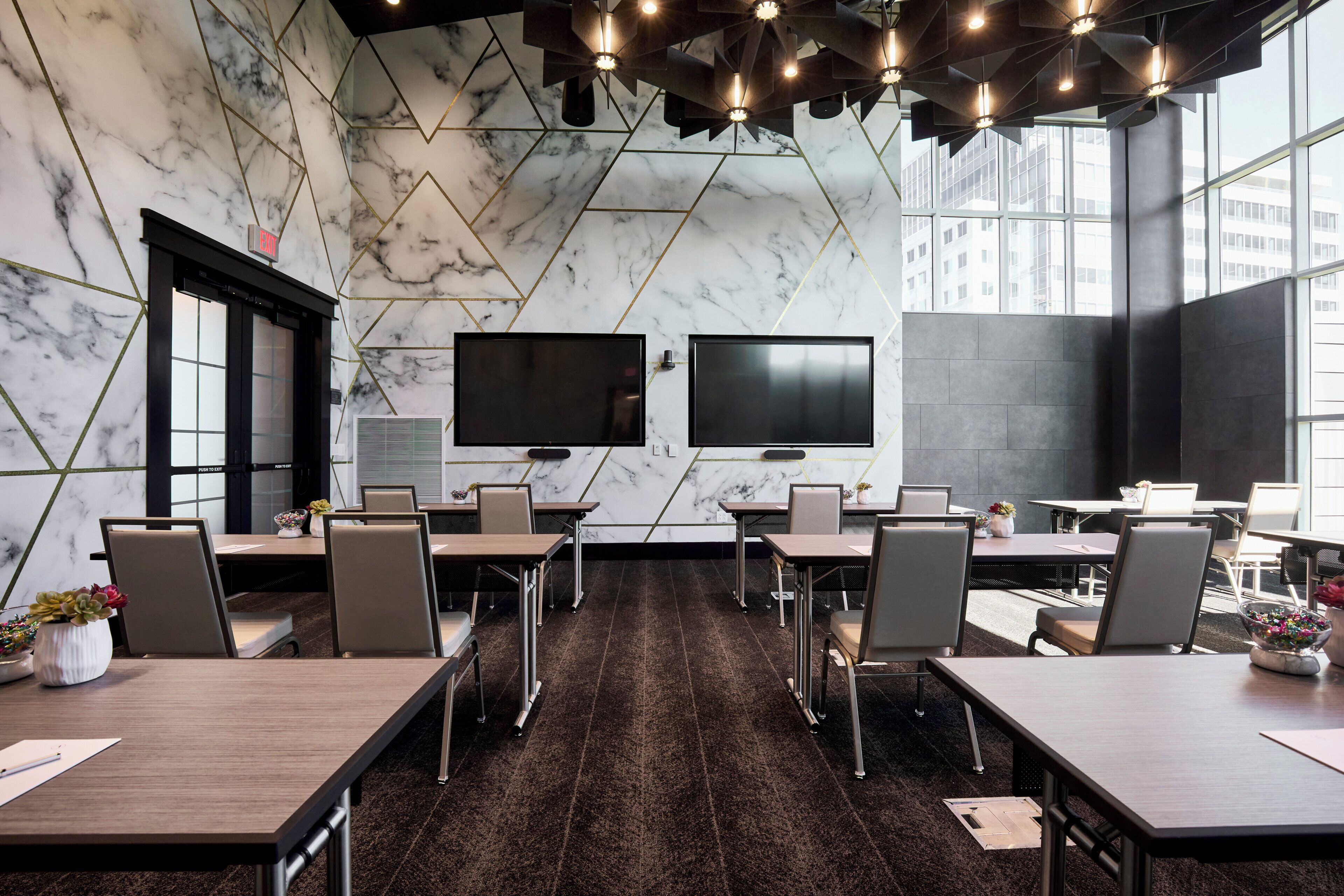 A modern conference room with marble walls, two large flat-screen TVs, and a long table with chairs.