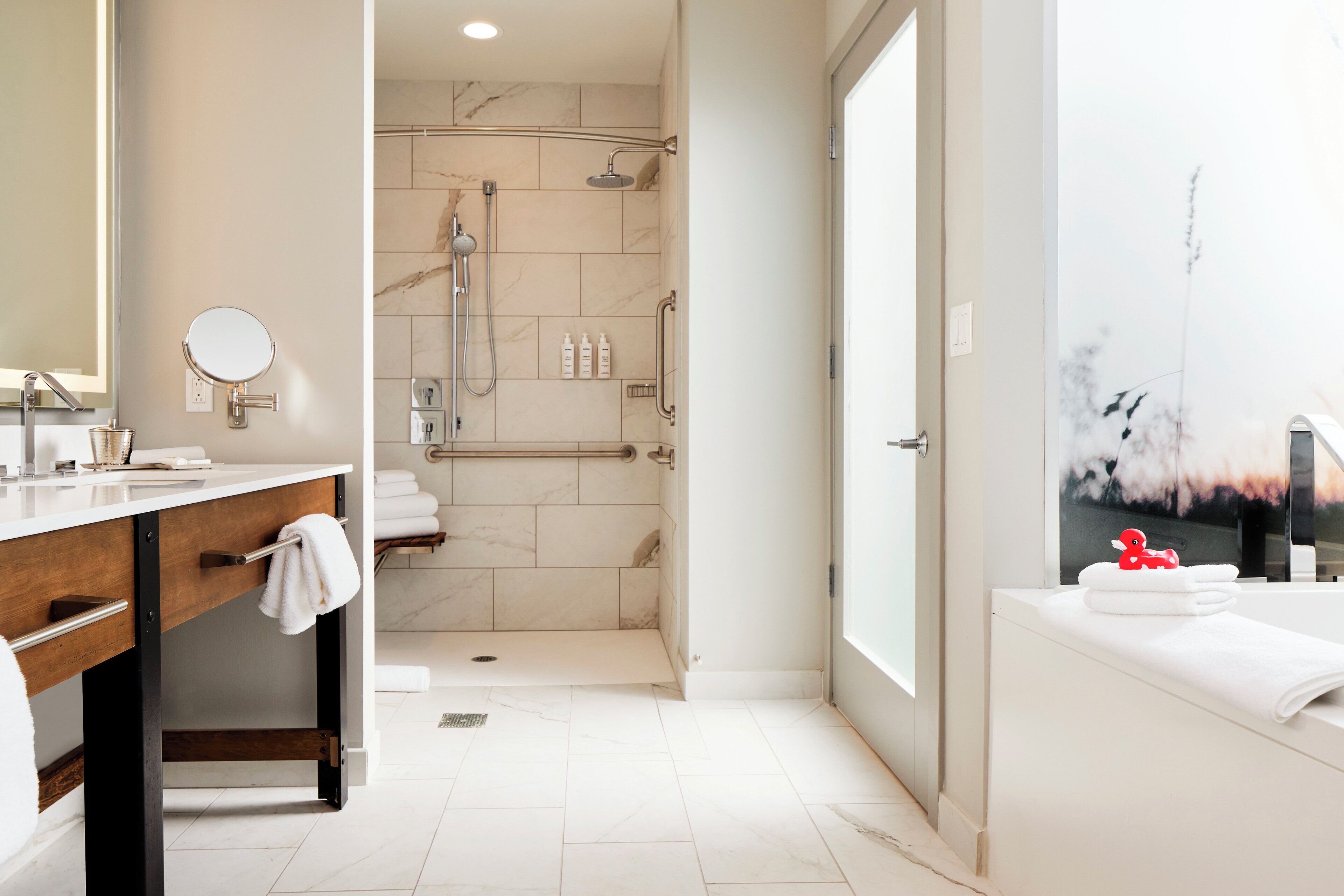 A modern bathroom with a vanity, a shower, and a large window with a view of birds.