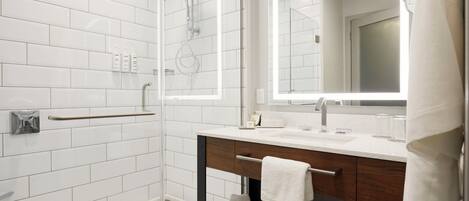 A modern bathroom with white subway tiles, a glass-enclosed shower, a wooden vanity with a towel rack, and a large mirror.