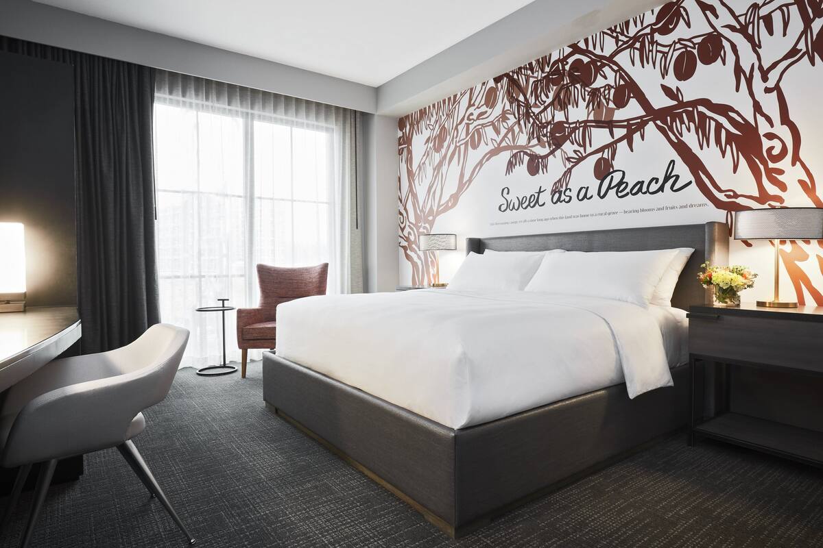 A hotel room with a large bed, a desk, a chair, and a wall mural.