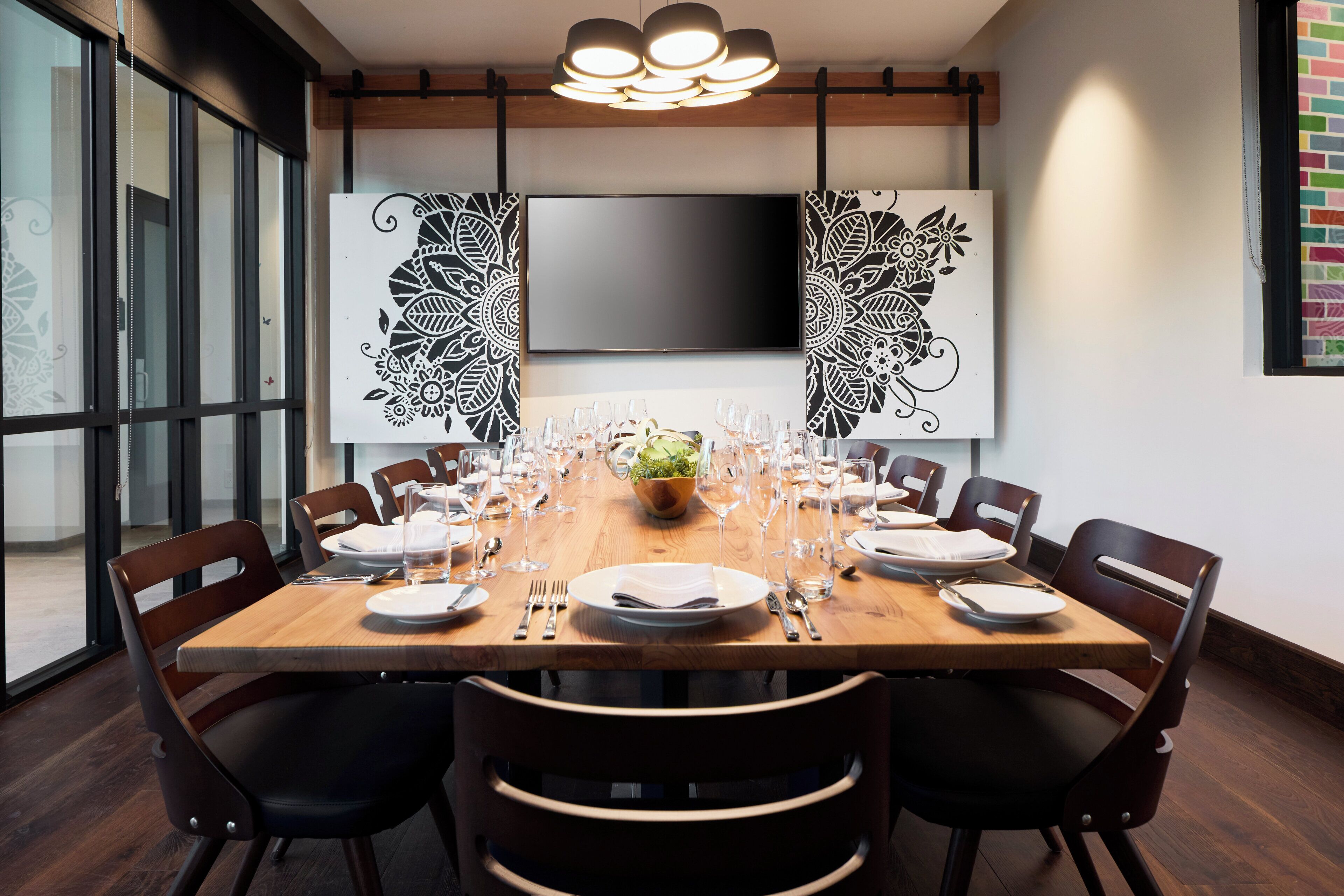 A conference room with a long table set for a meeting, surrounded by chairs, a flat-screen TV, and decorative wall art.