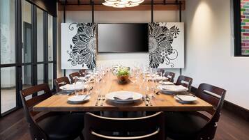 A conference room with a long table set for a meeting, surrounded by chairs, a flat-screen TV, and decorative wall art.