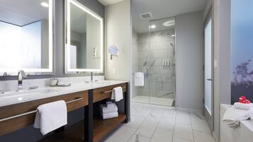 A modern bathroom with two sinks, a large mirror, a glass shower enclosure, and marble flooring.