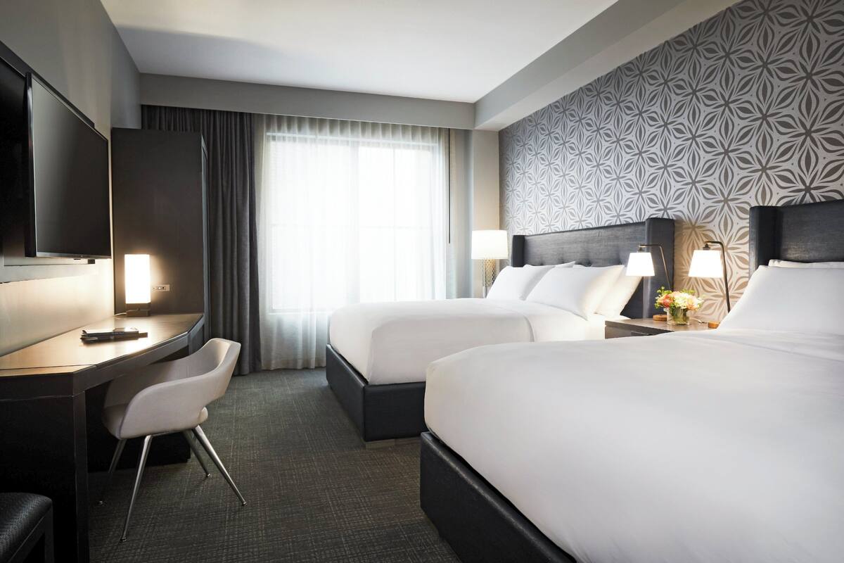 A hotel room with a desk, two beds, a TV, and a patterned wall.