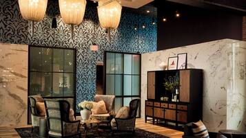 A modern lobby with patterned wallpaper, a marble fireplace, and a seating area with armchairs and a coffee table.