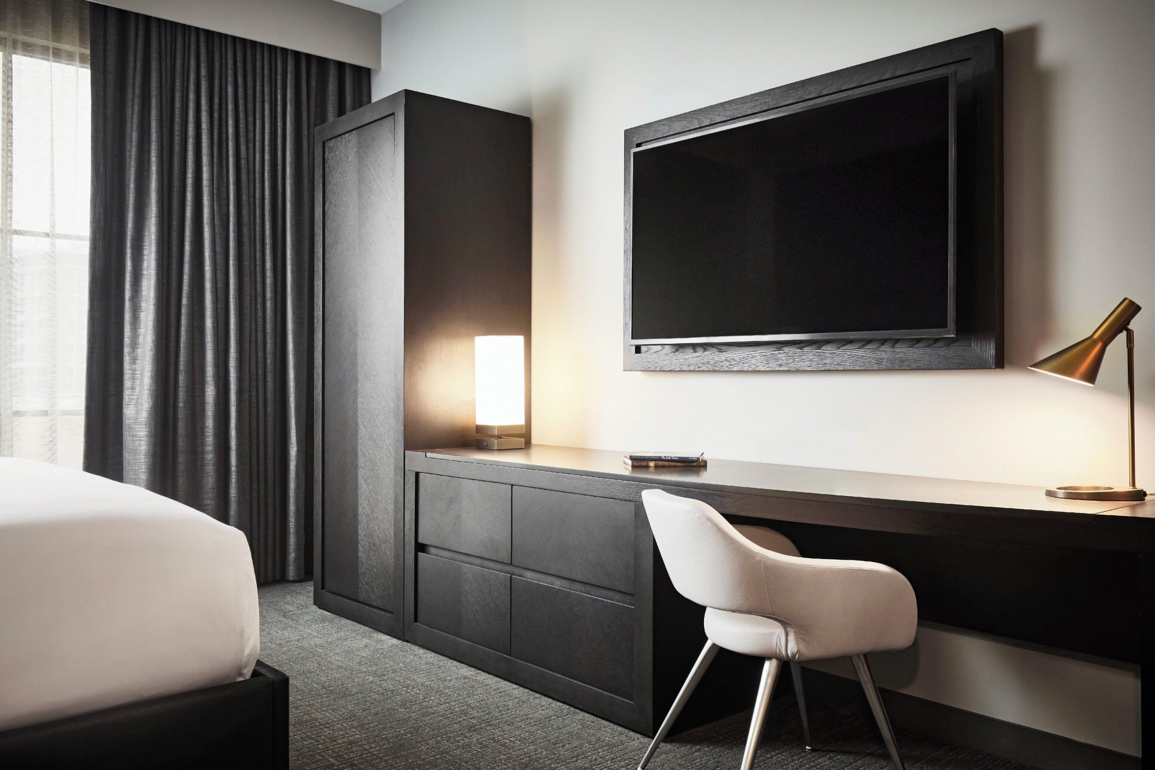 A hotel room with a bed, a desk with a chair, a television, and a lamp.