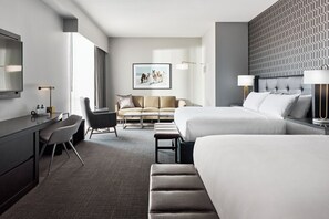 A hotel room with a large bed, a sofa, a desk, and a chair. There is a framed picture on the wall and a lamp on the desk. - Archer Hotel Tysons (McLean)