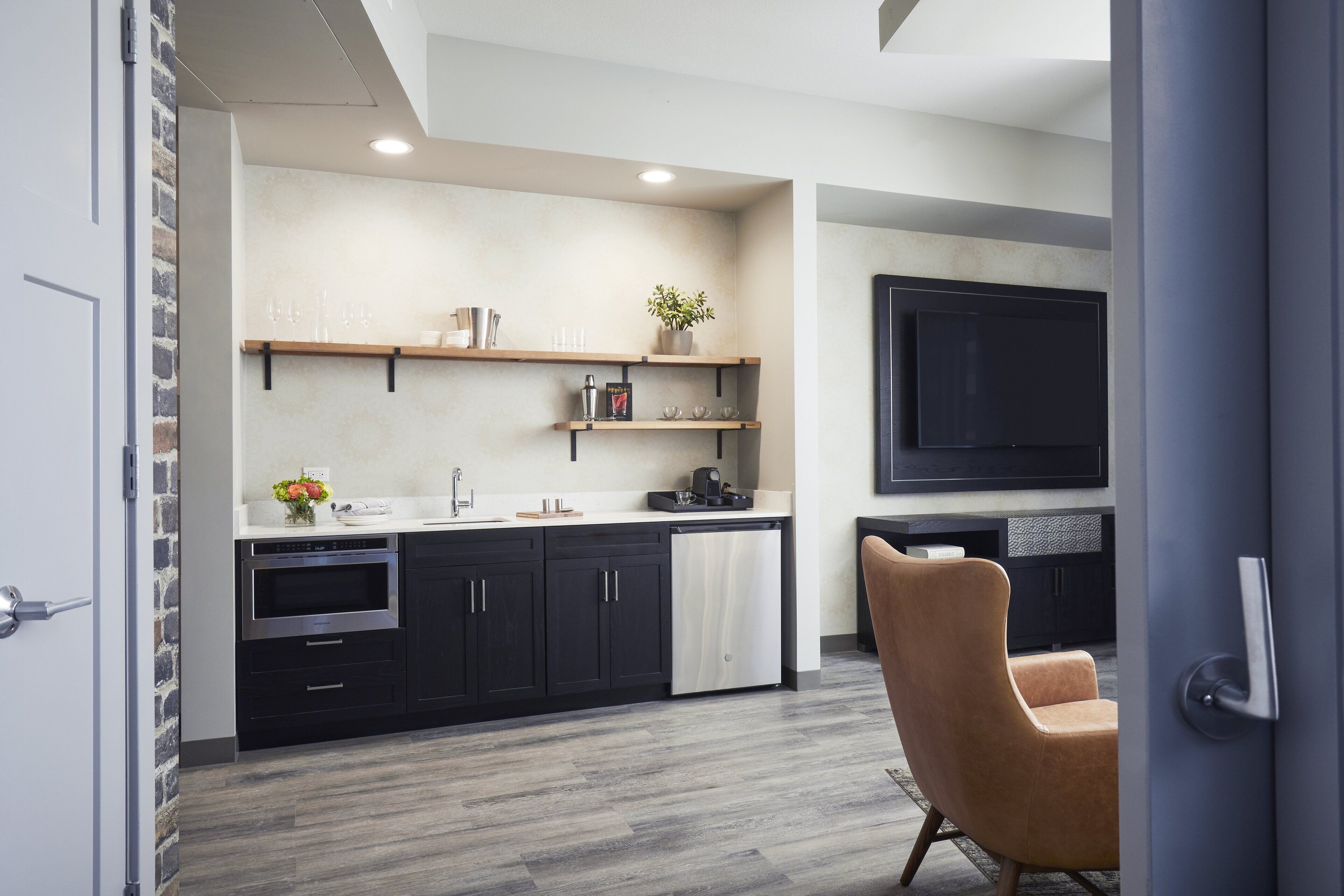 Una cocina moderna con muebles oscuros, horno empotrado y encimera con diversos objetos.