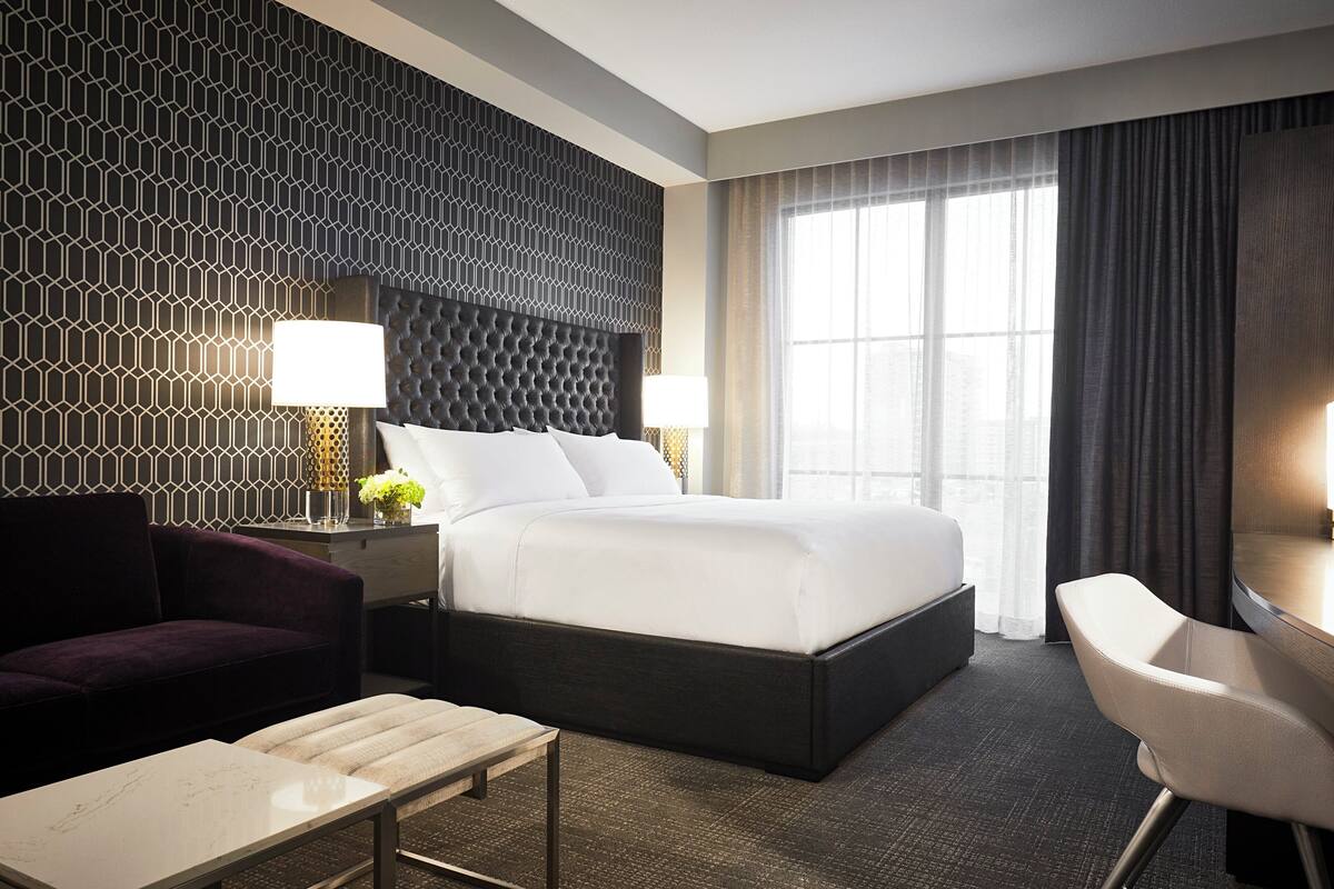 A hotel room with a large bed, a sofa, a desk, and a window with curtains.
