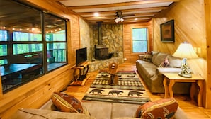 A cozy cabin interior with a stone fireplace, wooden furniture, and large windows offering views of the forest. - ★Cozy Log Cabin★ Secluded, modern amenities, mins to dwtwn Blueridge. Pets OK! (Blue Ridge)