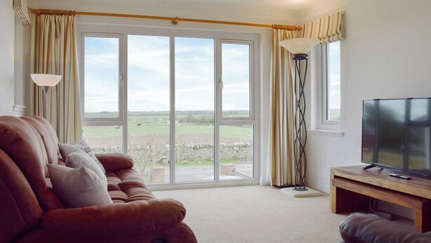 A living room with a sofa, a TV, and a large window with curtains.
