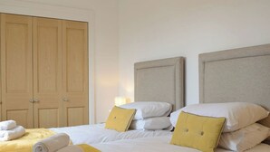 A hotel room with a large wooden wardrobe, a bed with white bedding and yellow pillows, and a yellow throw blanket.