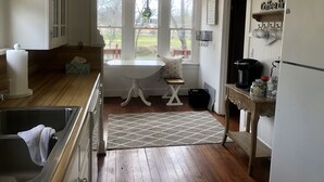 Una cocina con un lavamanos, una mesa y un refrigerador. Se ve una ventana con vistas al exterior.