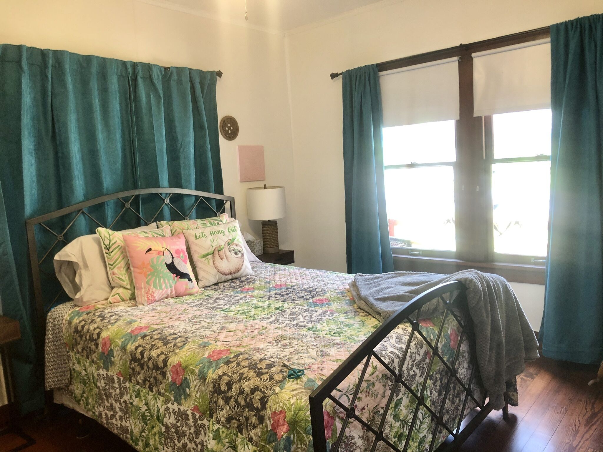 A bed with a floral bedspread, a headboard, and two pillows with animal prints. There is a bedside table with a lamp and a wall clock.