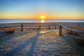Ein Strandweg, der zum Meer führt, mit einem Sonnenuntergang im Hintergrund.