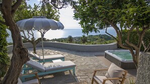 Une terrasse avec des chaises longues, une table en bois, un jacuzzi et une vue sur la mer.