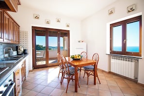 Un comedor con mesa y sillas, una cocina con armarios y electrodomésticos, y una vista por una puerta.