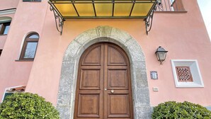 Un bâtiment doté d’une grande porte à double battant en bois, d’une arche en pierre et d’un auvent jaune. De part et d’autre de la porte, on trouve deux plantes en pot.