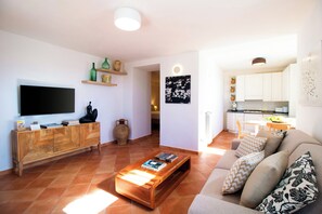 Una sala de estar con televisor de pantalla plana, mesa de centro de madera y un sofá con cojines estampados.