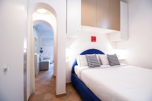 Una habitación de hotel con una cama, un cabecero azul y una pared blanca con detector de incendios rojo.