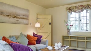 A cozy living room with a light-colored sofa, colorful cushions, a wooden coffee table with tea cups, a lamp, and a window with a floral curtain. - 2 bedroom accommodation in Preston Crowmarsh, near Wallingford (Preston Crowmarsh, near Wallingford)