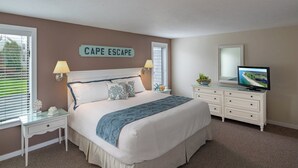 Et soveværelse med en seng, to sengeborde, en kommode, et fjernsyn og et skilt med teksten "CAPE ESCAPE".