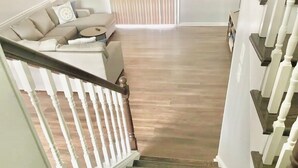A staircase with a wooden finish and white balusters, leading to a room with a beige sofa and a small round table. - Sleeps 10! Brand new kitchen & main bathroom! Highly sought after 4bd,3ba. (Smyrna)