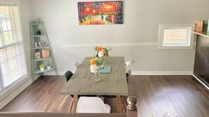 A dining area with a wooden table, chairs, and a vase of flowers. There is a shelf with decorative items and a painting on the wall. - Sleeps 10! Brand new kitchen & main bathroom! Highly sought after 4bd,3ba. (Smyrna)