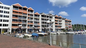 Un hotel frente al agua con varios balcones, un puerto deportivo lleno de barcos y un cielo azul despejado.