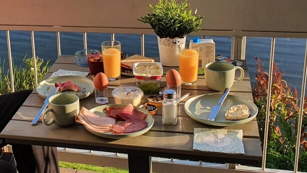 Una mesa de desayuno con diversas comidas y bebidas, con vista a un cuerpo de agua.
