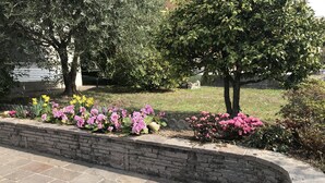Un jardin aménagé avec un muret en briques, diverses plantes à fleurs et des arbres.