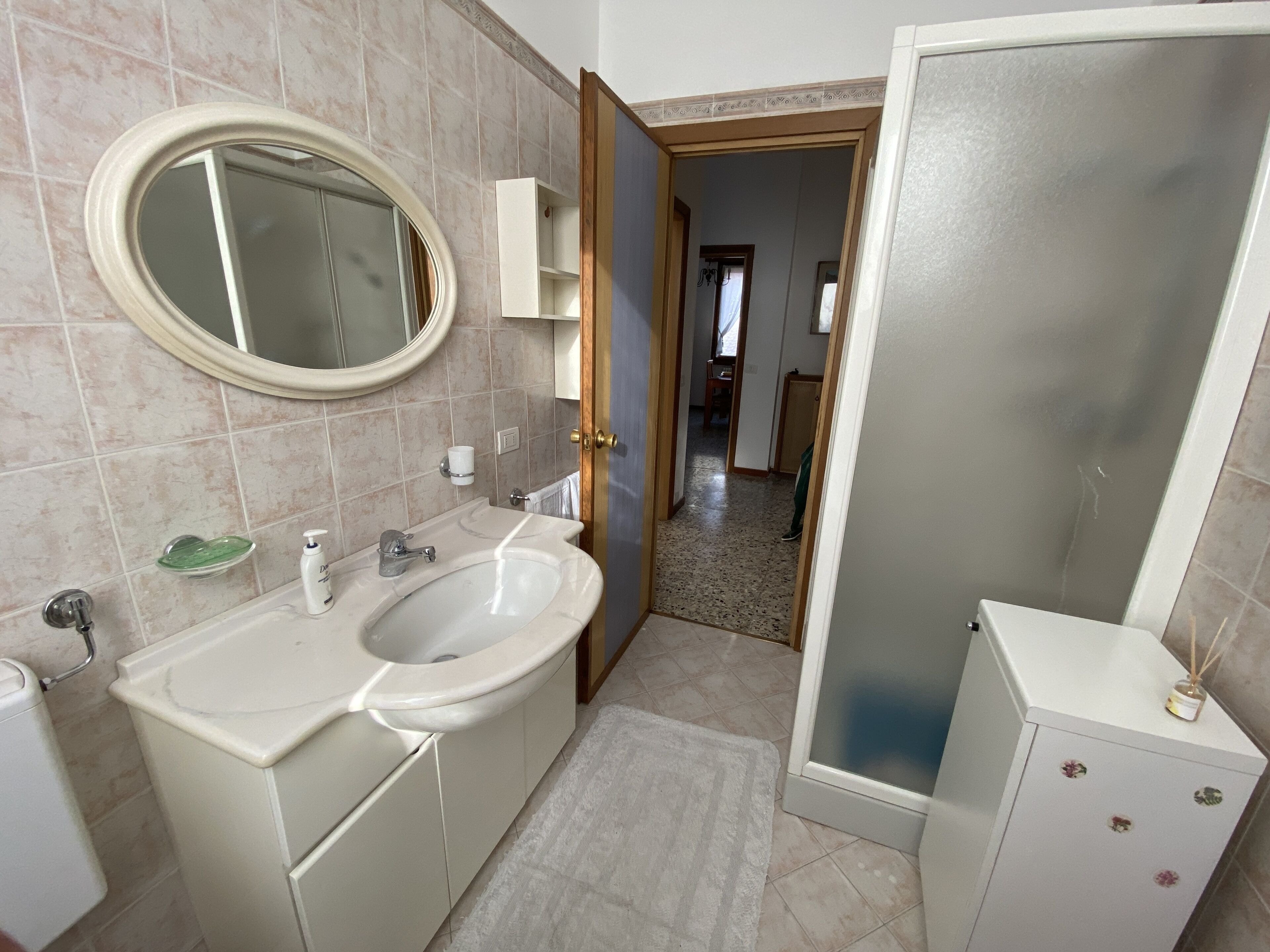 Une salle de bain avec un lavabo blanc, un miroir et des toilettes. Un porte-serviettes et un distributeur de savon sont fixés au mur.