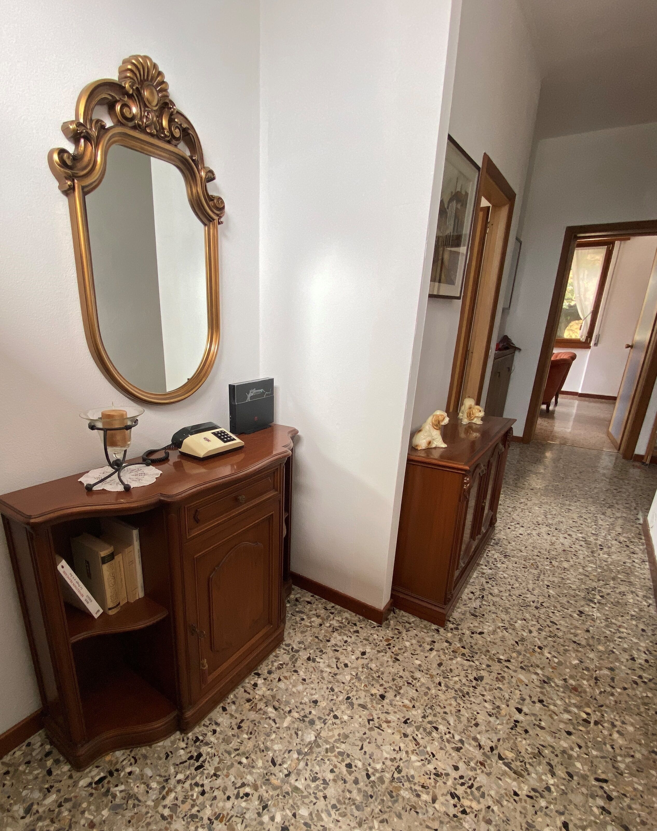 A hallway with a wooden vanity, a large mirror, and a small table with a telephone and a box.