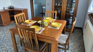 Un coin repas avec une table en bois dressée pour quatre personnes, entourée de chaises. On aperçoit un meuble avec des portes en verre à l’arrière-plan.