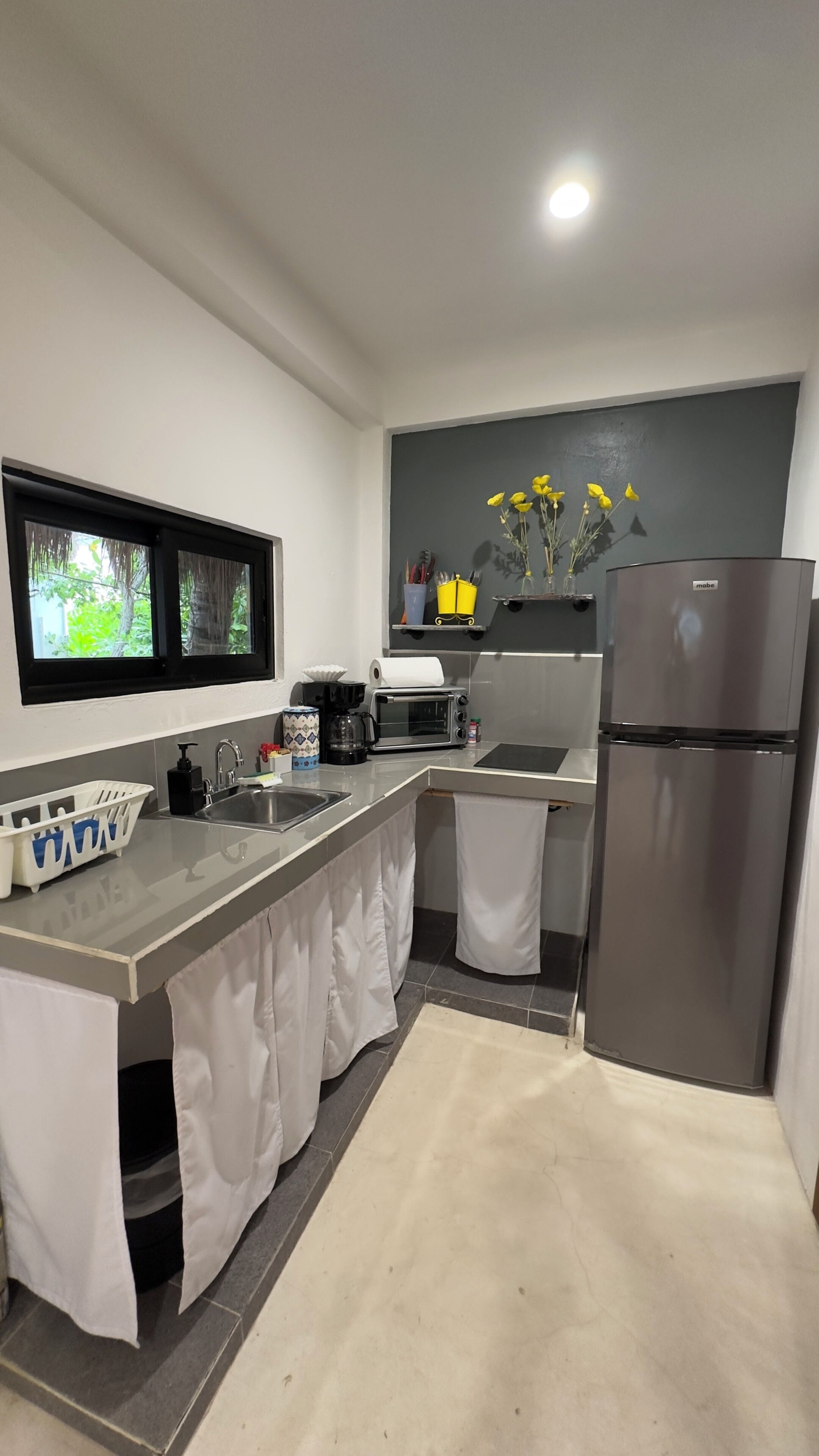 A modern kitchen with a built-in oven, a refrigerator, and a window overlooking greenery.