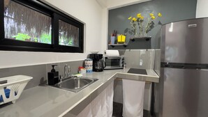 A modern kitchen with a stainless steel refrigerator, a coffee maker, a toaster, and a window with a view of greenery.