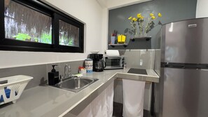 A modern kitchen with a stainless steel refrigerator, a coffee maker, a toaster, and a window with a view of greenery.
