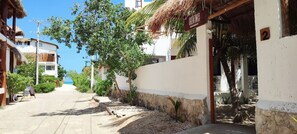 A narrow street with buildings on either side, a thatched-roof structure, and a sign indicating a location.
