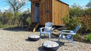 Una cabaña de madera con puerta, chimenea y un pequeño porche con dos sillas y dos cojines.