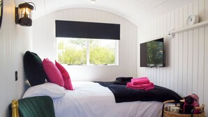 Un dormitorio con cama, televisión, ventana, mesita de noche y una silla.