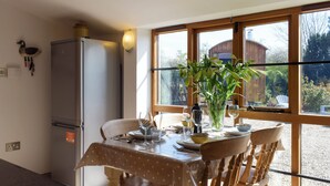 Un comedor con una mesa dispuesta para cuatro personas, un refrigerador y una ventana con vistas a un edificio y árboles.