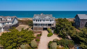A coastal house with a large deck, a covered driveway, and a view of the ocean. - Chez la Mer – Oceanfront 5BR Sanderling Home with Private Walkway & Big Views (Duck)