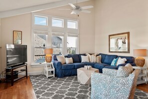 A living room with a sectional sofa, a flat-screen TV, and a large window with multiple panes.