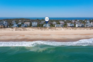 A coastal residential area with houses along the beachfront, a clear sky, and a calm sea.